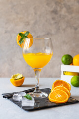 Yellow bird cocktail made with rum, ice, orange and lime juice in glass. Fruits in box, ice cubes, stone board on concrete background