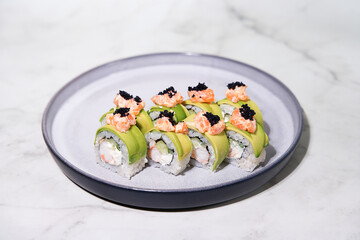 Closeup sliced rolls with shrimp in avocado, with salmon and black caviar on a plate, selective focus