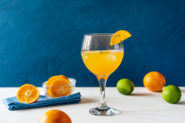 Yellow bird cocktail with rum, orange and lime juice, oranges and limes, blue napkin. White table. Dark blue background