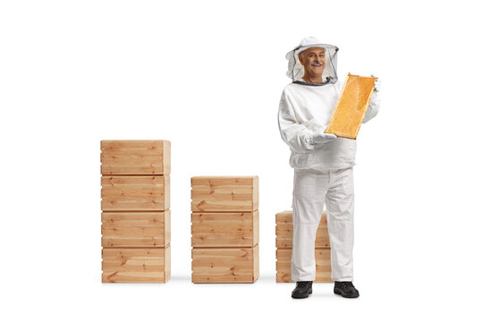 Full length portrait of a bee keeper in a uniform holding a honeybee frame in front of wooden boxes