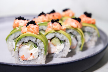 Closeup sliced rolls with shrimp in avocado, with salmon and black caviar on a plate, selective focus