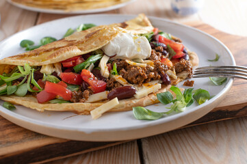 Ground beef dish with a fresh pancake or crepe filled with kidney beans, vegetables, cheese and topped with sour cream