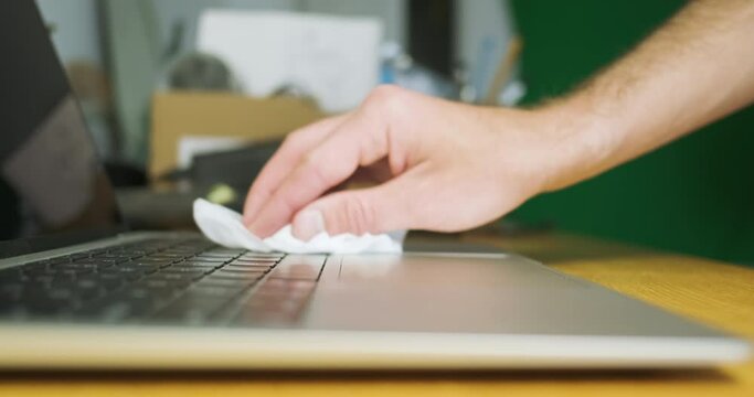 Man's hand wipes the laptop keyboard from dust with damp cloth. Concept caring for laptop, disinfection, kill germs, health, care for things.