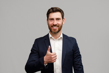 Portrait of smiling businessman riding his thumb up over grey studio background