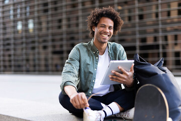 Young man with curly hair using digital tablet. Man sitting outside taking a break.