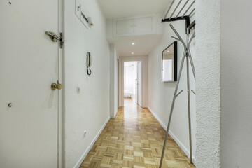 Entrance hall of a house with a long hall with a light varnished oak floor, white wooden doors, a metal coat rack and access to several rooms