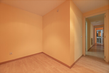 Empty room with peach painted walls and long hallway with light oak floorboards