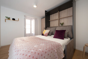 Furnished studio apartment with pull out fold out sofa bed, gilt shelving and pink polka dot blanket and hardwood floors.