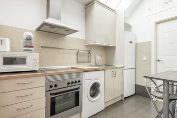 Fototapeta premium Open kitchen of an apartment with bright cream cabinets, stainless steel appliances and wooden countertops