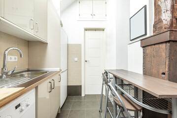 Open apartment kitchen with gloss cream cabinets, stainless steel appliances and wood countertops and sloping ceilings