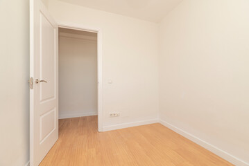 Empty room with light oak parquet flooring, plain white painted walls and white lacquered wooden door