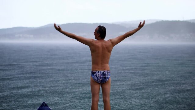 Back View Of A Man In Swimsuit Standing With Arms Outstretched At The Beach. full shot