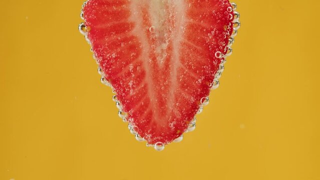 Strawberry in carbonated water. Cooking sweet cocktail, fizzy summer drink, cold lemonade with red berries, ripe fruits on yellow background.