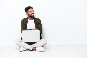 Young Brazilian man with a laptop sitting on the floor isolated on white happy and smiling