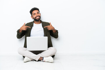 Young Brazilian man with a laptop sitting on the floor isolated on white proud and self-satisfied