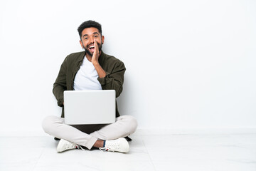Young Brazilian man with a laptop sitting on the floor isolated on white shouting with mouth wide open