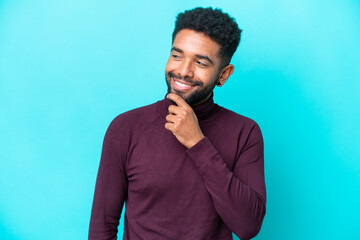 Young Brazilian man isolated on blue background looking to the side and smiling
