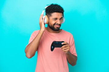 Young brazilian man playing with a video game controller isolated on blue background frustrated and...