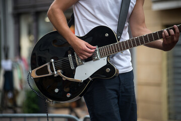 closeup of guitarist playing guitar with rock group in the street - obrazy, fototapety, plakaty