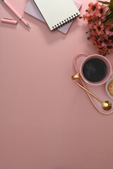 Flat lay blank notepad, coffee cup and flower pot on pink background. Top view, feminine workspace