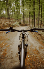 Fototapeta na wymiar Mountain bike handlebar viewed from the first-person perspective. visible bicycle frame and bicycle accessories on the handlebar and the forest trai. Concept of spending time outdoors while bikeriding