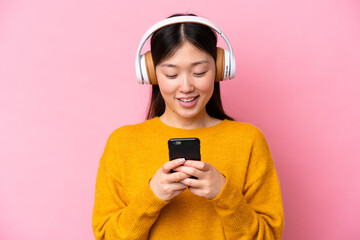 Young Chinese woman isolated on pink background listening music and looking to mobile