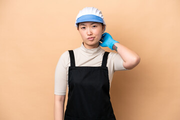 Young Chinese Fishmonger woman wearing an apron and holding a raw fish isolated on pink background having doubts