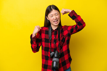Young photographer Chinese woman isolated on yellow background celebrating a victory