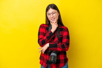 Young photographer Chinese woman isolated on yellow background with glasses and smiling