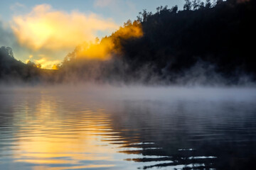 Mountains lake silhouettes in sunrise. Foggy blue dreamy landscape of Kumbolo lake, Mount Semeru,  Indonesia