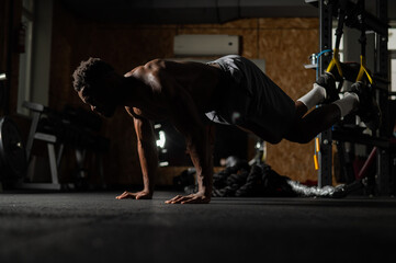 Shirtless afro american man doing exercises with functional loops in the gym. 