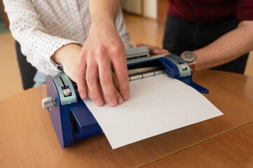 A man teaches a blind woman to type on braille machine.  - obrazy, fototapety, plakaty