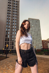 Outdoor close up portrait of young beautiful woman in shorts and top posing against city background.