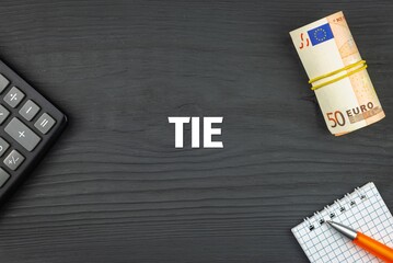 TIE - word (text) and euro money on a wooden background, calculator, pen and notepad. Business concept (copy space).