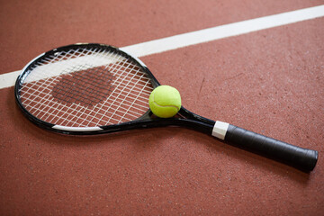 Close-up of tennis racquet and green ball placed on red floor of tennis court, copy space - Powered by Adobe