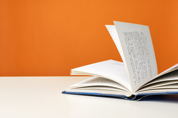 Open book on a white table against color background.