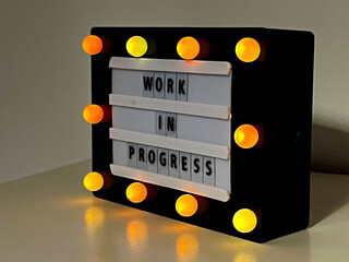 Work in Progress sign in diagonal position with small yellow lights around it.
