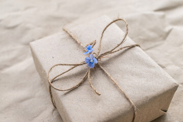 A gift in craft packaging with a rope bow. Decorated with a blue flower. Summer gift wrapping. Holiday. Eco-friendly gift wrapping. Ecology. Postcard for the holiday. Close-up. selective focus.