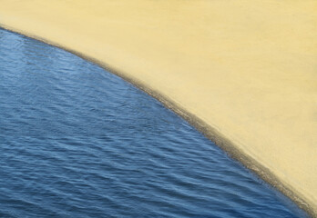 Texture of blue water and beach with yellow sand