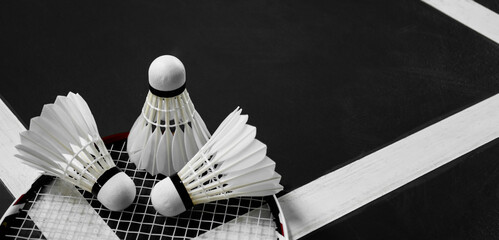 White cream badminton shuttlecock  and rackets on dark floor of the indoor badminton court, soft...