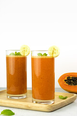 Orange papaya and banana smoothie mix on white background, copy space. A glass of fresh papaya and banana smoothie.