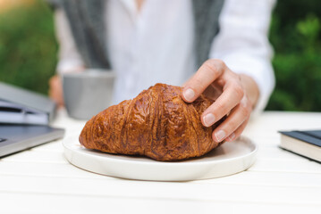 Unrecognizable female hand holds a freshly baked croissant.
