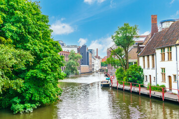 Fototapeta na wymiar Ghent, Belgium. A picturesque canal with old houses and a boat on the pier in summer under a blue sky with clouds.