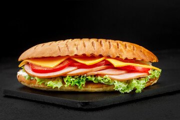 Sandwich with pastrami and cheese and tomatoes and salad in the dark background