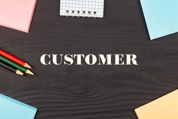 CUSTOMER - text, stickers and colored pencils on a black wooden table. Business concept: buying, selling, commerce (copy space).