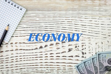 Naklejka premium ECONOMY - word (text) and dollars on a white wooden table, notebook, notepad. Business concept: buying, selling, commerce (copy space).