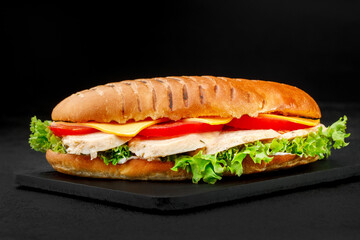 Sandwich with chicken and cheese and tomatoes and salad on a dark background