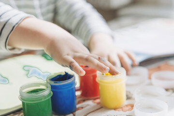 Finger painting. Cute little boy painting with fingers at home. Close-up of child's hand in colorful paints. Early education concept. Sensory play. Development of fine motor skills.