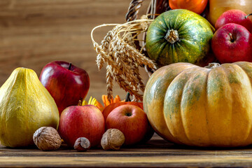 Thanksgiving day close up still life. Pumpkin harvest in wicker basket. Squash, vegetable autumn fruit, apples, and nuts on a wooden table. Halloween decoration fall design