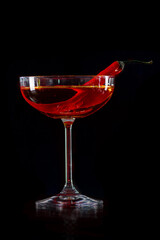 Cocktail with hot chilli pepper on bar counter in a restaurant, pub. Fresh spicy drink. Alcoholic cooler beverage on isolated black background